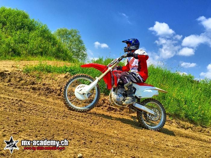 Sport d’action pour tous : pilote au casque bleu sur une moto de motocross Honda dans la pente de la piste Sport d’action pour tous : pilote au casque bleu sur une moto de motocross Honda dans la pente de la piste