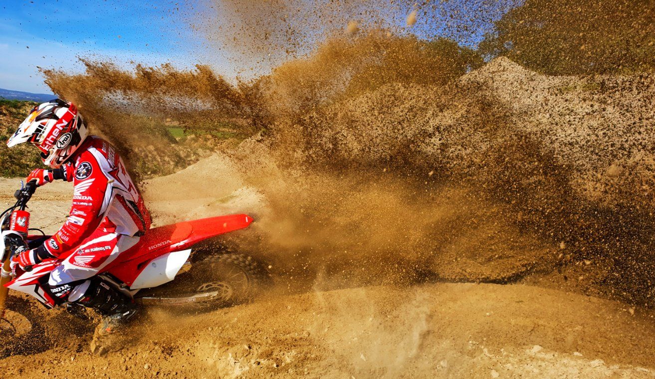 Activité insolite en Suisse : pilote de motocross sur une Honda dans un virage de sable avec une haute gerbe de sable Activité insolite en Suisse : pilote de motocross sur une Honda dans un virage de sable avec une haute gerbe de sable