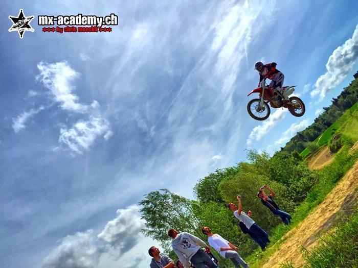 Sport d’action en Suisse : pilote de motocross en plein saut, des spectateurs photographient au bord de la piste Sport d’action en Suisse : pilote de motocross en plein saut, des spectateurs photographient au bord de la piste